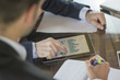 © GENETTICA - Business meeting. The finger of a young man pointing at the screen of a tablet with information displayed in graph form. His coworker is taking notes in a notebook. All screen graphics are made up.