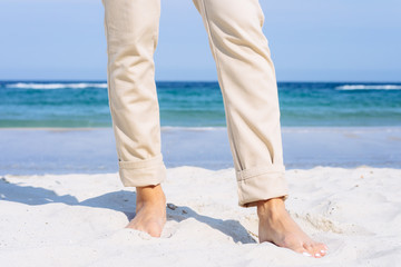 Wall Mural - Close-up of female legs in beige pants barefoot on the beach