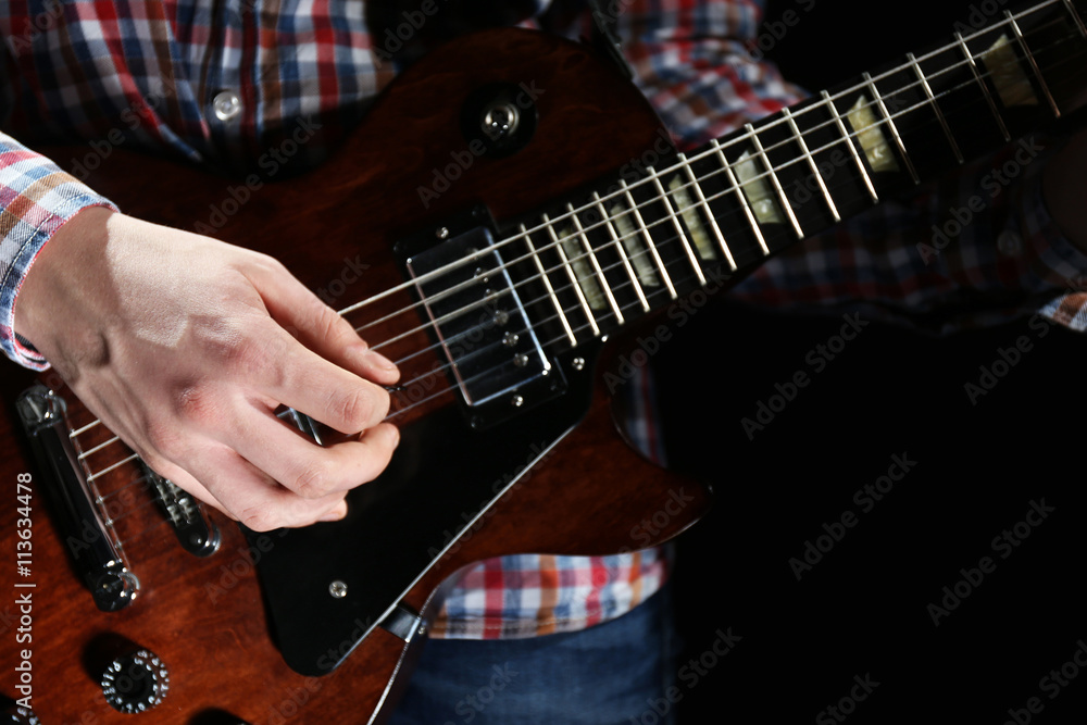 Young man playing electric guitar on lighted dark background