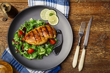 Wall Mural - Grilled chicken breast with green salad on a black plate.
