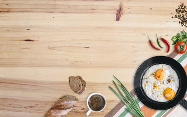 Farmers breakfast. Frying pan with two fried eggs, tomato, green onion, chili and black pepper, bread and coffee on aged wooden table. Top view with copy space