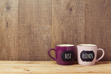 Wall Mural - Coffee cups on wooden table with chalkboard sign and best friends text. Friendship day celebration background