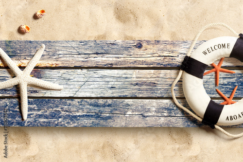 Board z aluminiowym obramowaniem Lifebuoy i morskie życie na starych drewnianych deskach na piasek plaży