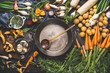 Various organic vegetables ingredients around empty aged cooking pot with wooden spoon on old kitchen table, top view