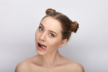 Portrait of a young woman with funny hairstyle and bare shoulders act the ape showing tongue against white studio background