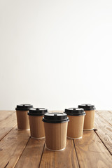 Wall Mural - Five carton paper cups with black caps in row isolated on center of rustic wooden table, top view