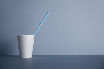 Wall Mural - One take away white paper cup without cap with blue drinking straw inside presented in left side, isolated on gray