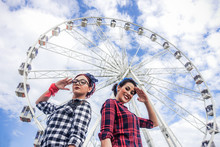Two Friends Posing In Camera With Ferris Wheel In Background 