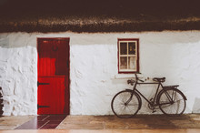 Traditional Irish Thatched Cottage, With Red Wooden Two Parts Door And An Old Bicycle