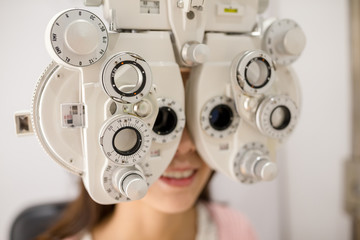 Canvas Print - Female patient looking through phoropter during eye exam