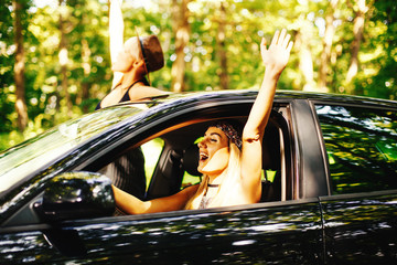 Wall Mural - Two Happy Young Woman Driving Along Woods Road in Black Car