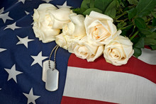 Military Dog Tags And White Rose Bouquet On American Flag.