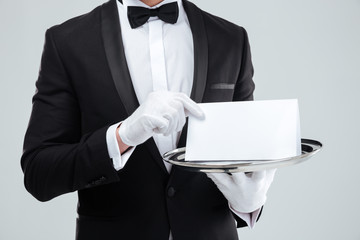 Butler in tuxedo and gloves holding blank card on tray