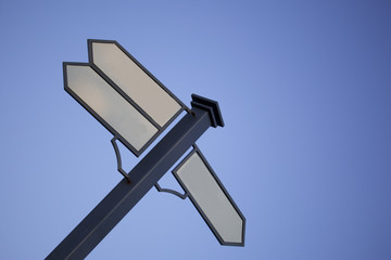 Signpost. Index path, located on the pole. Black metal pole. Arrows with a white field for writing. Against the background of the blue sky.