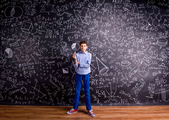 Boy against big blackboard with mathematical symbols and formula
