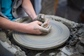 Child learning clay pottery, hands on a wheel closeup