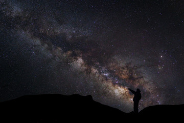 Wall Mural - a man is standing next to the milky way galaxy pointing on a bri