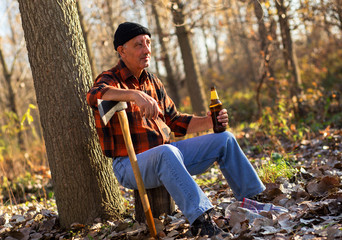 Poster - Senior lumberjack in forest. He is resting and drinking beer.