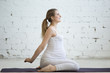 Pregnancy Yoga and Fitness. Portrait of young pregnant yoga model working out in loft. Pregnant fitness person smiling while practicing yoga at home. Prenatal Hero Pose, Virasana. Side view