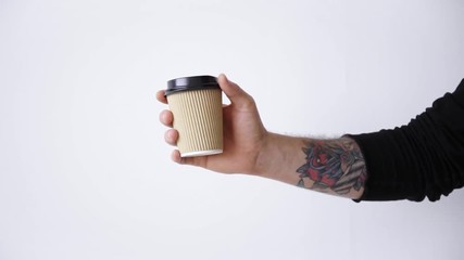 Wall Mural - Man tattooed hand in black longsleeve appears from right side with brown paper cup slow motion