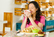 © Fotos 593 - Pretty brunette woman sitting at table inside bakery, holding cup of coffee and smiling happily, bread selection in front