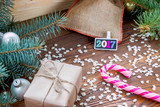 Fototapeta Lawenda - christmas gifts packaged in craft paper and black nameplate with colorful wood new year numbers, pink candy cane,  sprinkling as snowflakes on wooden table.