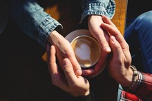 Overhead View Of Couple Holding Coffee Cup At Cafe