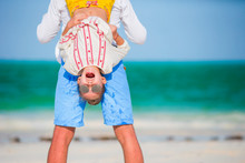 Happy Father And His Adorable Little Daughter At Tropical Beach Having Fun. Kid Hanging Upside Down In The Hands Of Her Dad