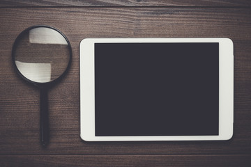 magnifying glass and tablet computer on brown wooden background