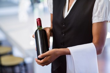 Wall Mural - Mid section of waitress holding a bottle of red wine and a towel