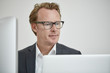© Westend61 - Portrait of businessman wearing glasses looking at computer