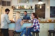 © WavebreakmediaMicro - Waiter looking at female customers sitting at counter in cafe