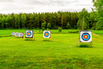 Outdoor archery targets on grass field surrounded by forest in the summer evening.