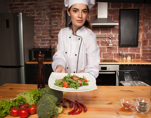 woman cook with fresh salad in her hands in kitchen interior