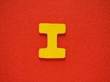 Fototapeta Desenie - Capital letter I. Yellow letter I from wood on red background. Alphabet vowel.