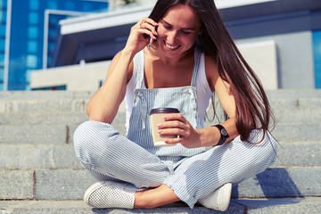 Wall Mural -  Woman in stylish overalls sitting on stairs with crossed legs a