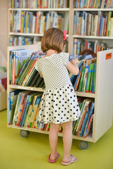 Little girl is choosing a book in the library.