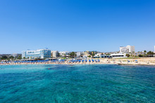 Photo Of Sea And Fig Tree Bay Beach In Protaras, Cyprus Island With Swimming People And Hotels.