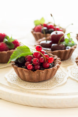 Wall Mural - Close up of chocolate tartlets with chocolate cream, fresh strawberries, raspberries, blueberries, red currants and cherries on white wooden background. Selective focus