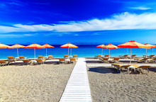 White Wooden Walkway On The Beach Including Umbrellas With Deck Chairs. Aegean Sea. Greece Rhodes. Pebble Beach