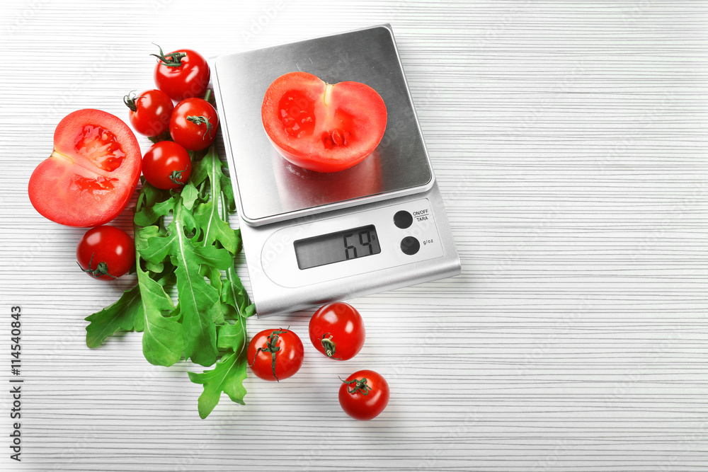Tomatoes with digital kitchen scales on wooden background
