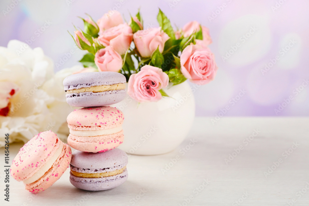Tasty macaroons with roses and peonies on wooden table