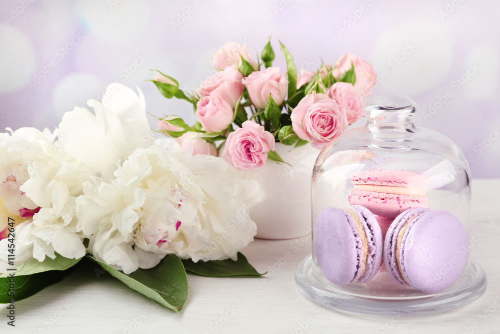 Tasty macaroons with roses and peonies on wooden table