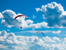 Two Dark Paraglide Silhouettes On Background Of Blue Summer Sky And White Clouds. Adrenalin Sport Theme.