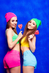 Wall Mural - Two beautiful hipster women with lollipops on blue background