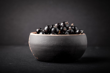 Currant berries in a clay bowl on black background. Selective fo