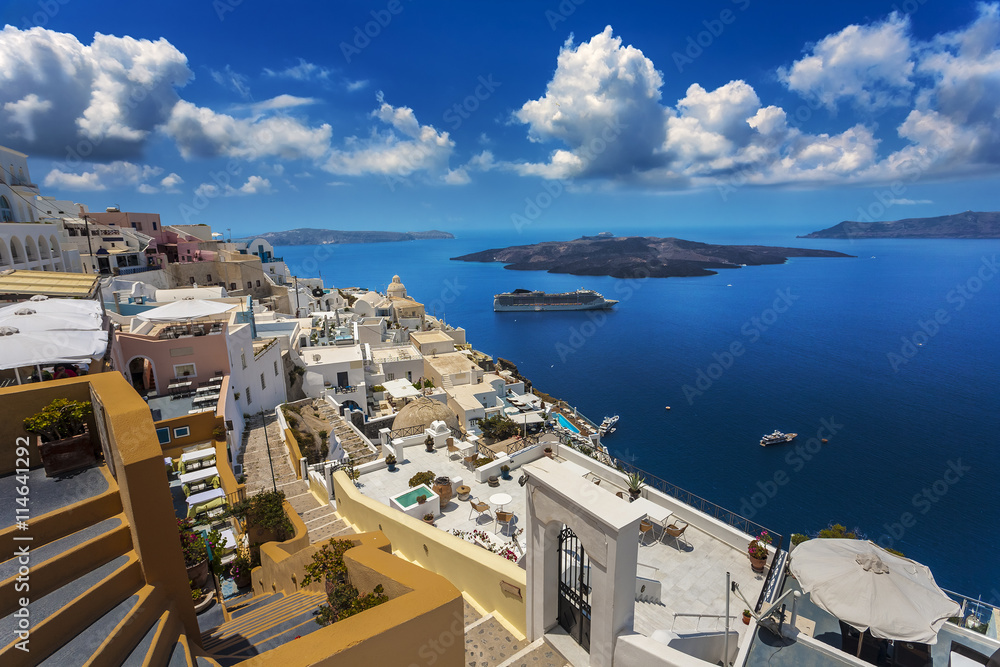 Greece. Santorini (Thira). Fira town with characteristic style for Cycladic architecture - white-washed cube houses built on the edge of high cliff. There is Nea Kameni Island in the background - obrazy, fototapety, plakaty 