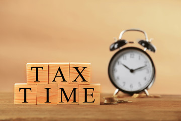 Sticker - Tax concept with wooden cubes, coins and alarm clock on light background