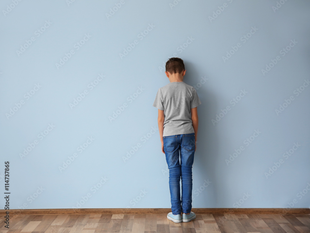 Family problems concept. Punished boy standing near wall