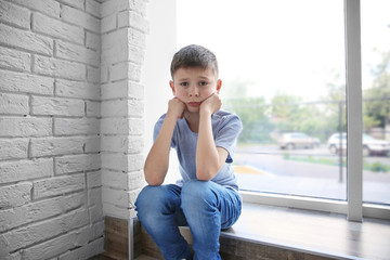 Wall Mural - Sad boy sitting near window